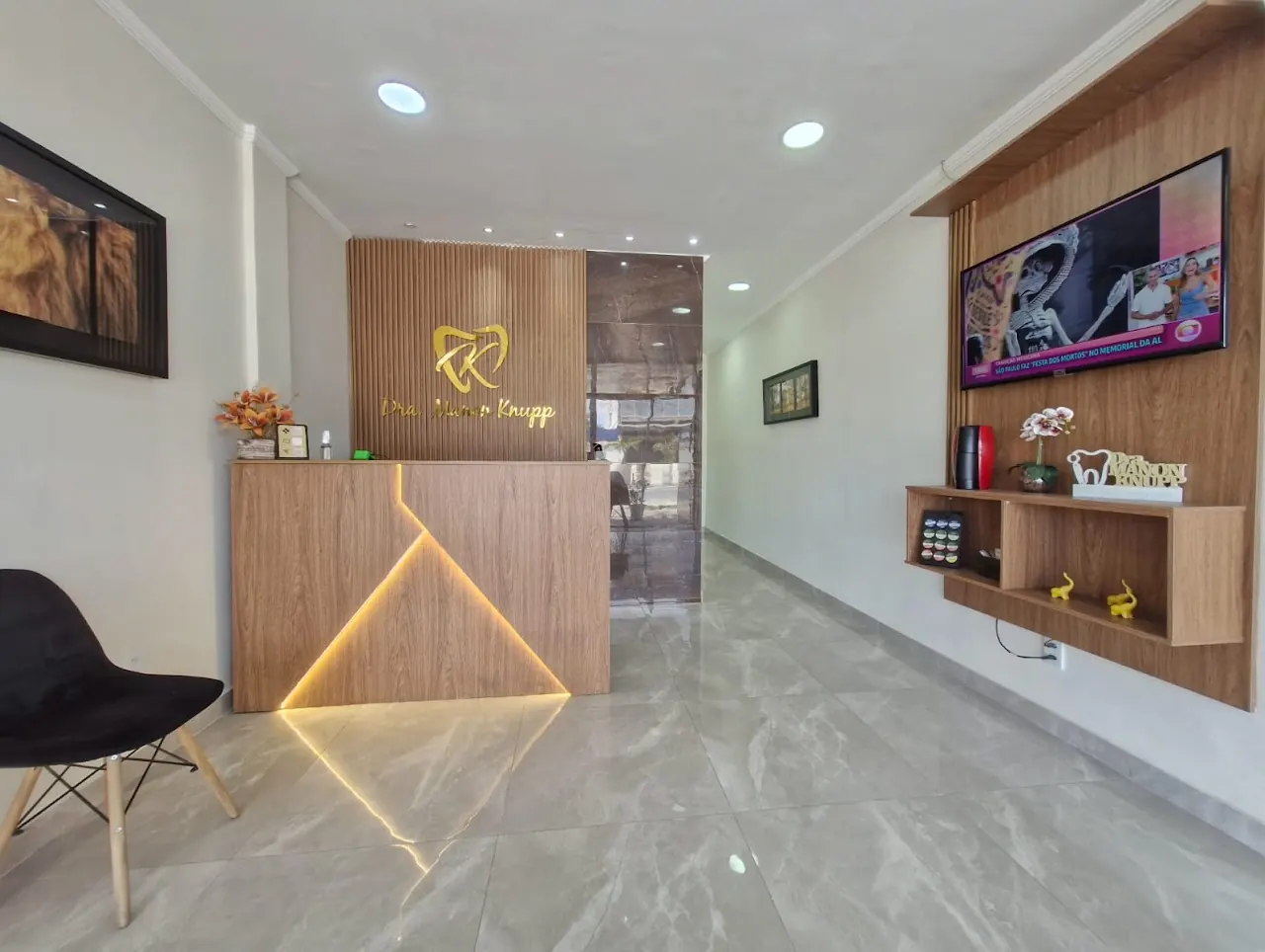 Recepção da Knupp Odontologia com balcão de madeira iluminado e logo dourado da Dra. Manon Knupp